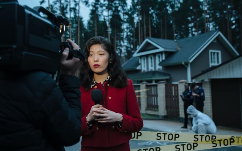 Female journalist reporting live from a crime scene with police and cameraman.