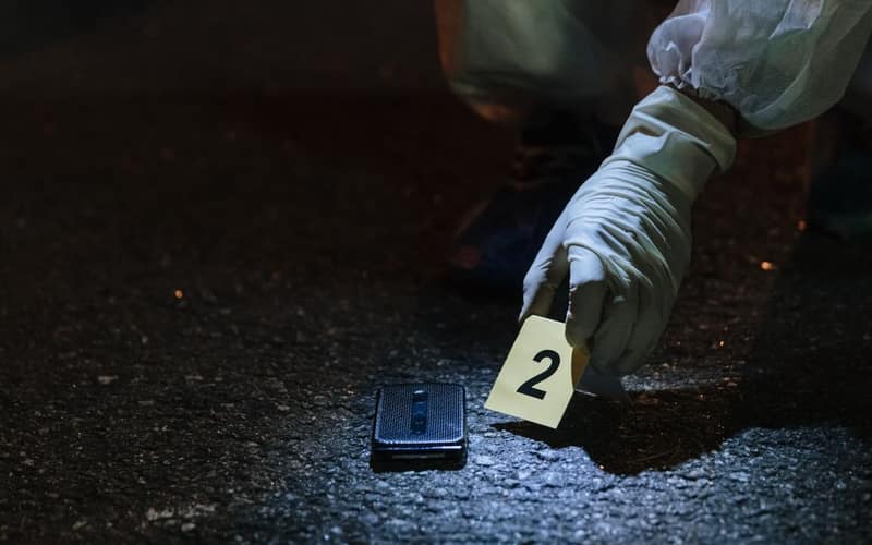 Forensic investigator examining evidence in a city street at night.