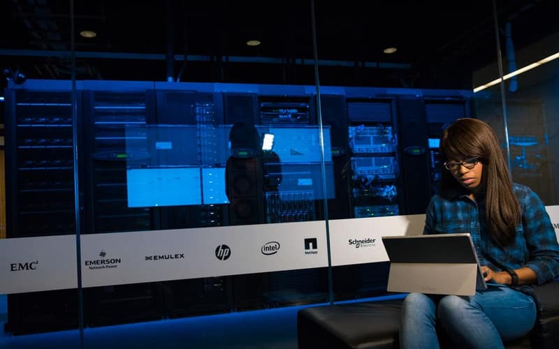 Woman using a laptop in a server room, showcasing modern technology and work environment.