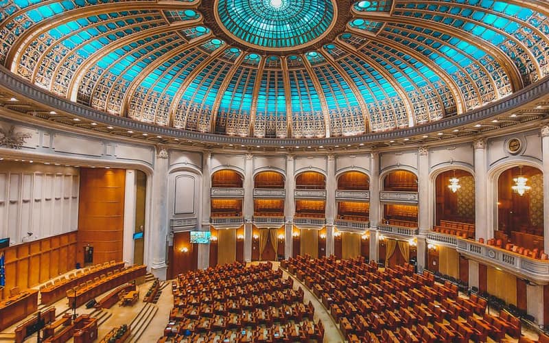 Vibrant interior of a parliament hall with a grand dome and intricate architecture.