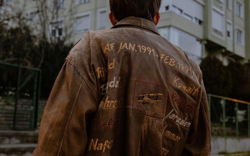 Back view of a man wearing a brown embroidered leather jacket standing in an urban setting.