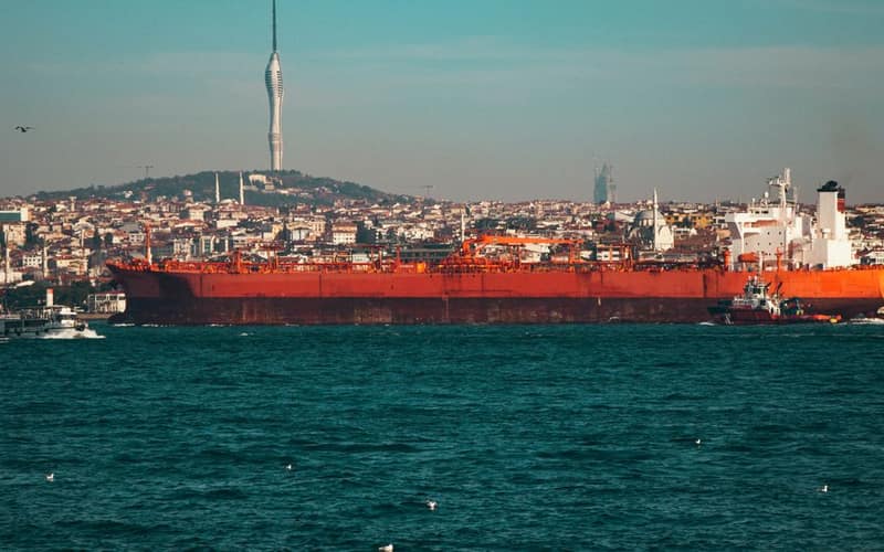 A large oil tanker navigates the Bosphorus Strait with Istanbul's skyline and Camlica Tower in the background.