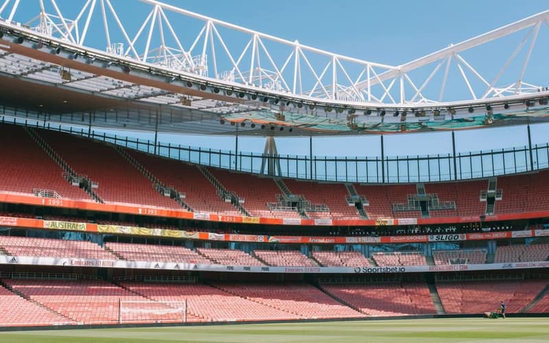 Wide view of Emirates Stadium's empty stands under a clear blue sky in London.