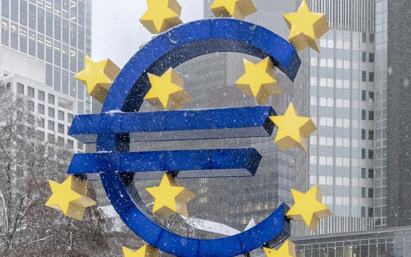 The iconic Euro symbol stands prominently amidst snowy Frankfurt skyscrapers.
