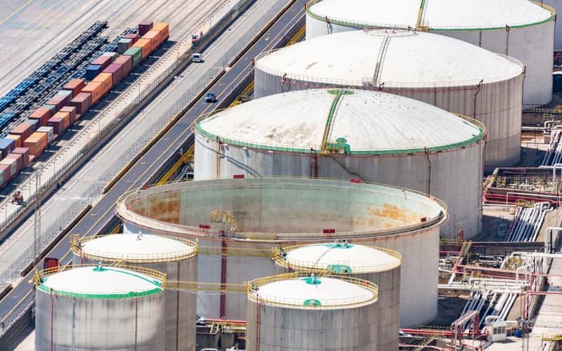 Aerial shot of large oil storage tanks in an industrial district with adjacent railway tracks.