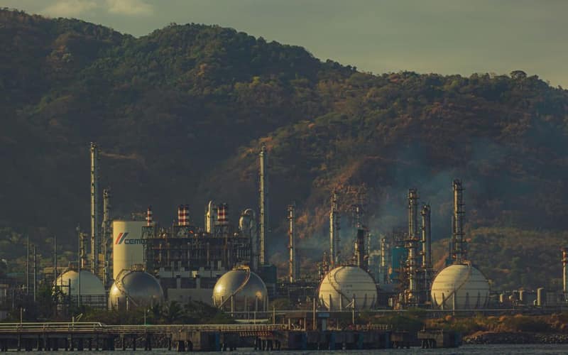 Industrial factory near mountains by a river, showcasing chimneys and infrastructure.