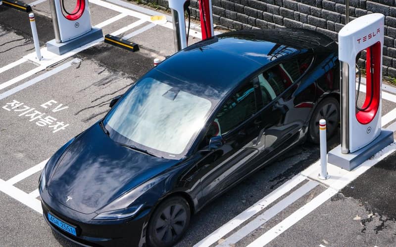 A black Tesla parked at a charging station in an urban setting.