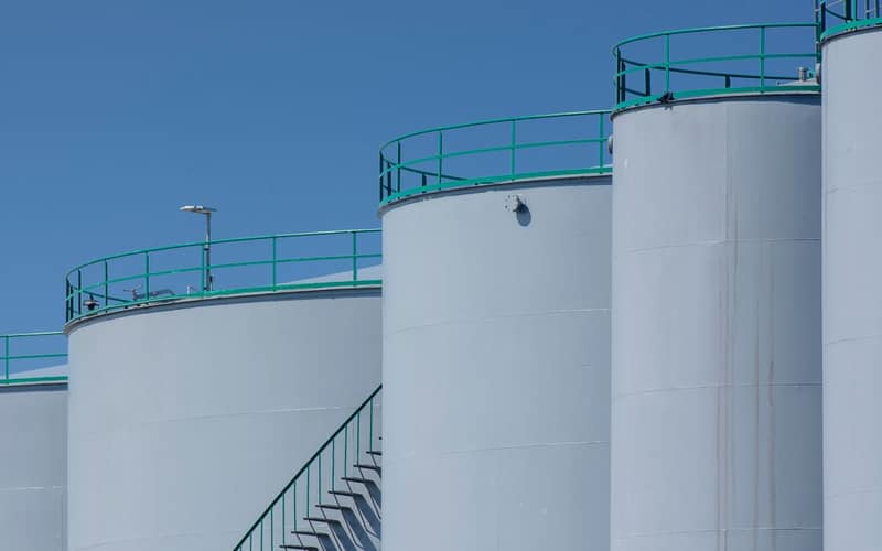 Large industrial storage tanks with green railings against a clear blue sky.