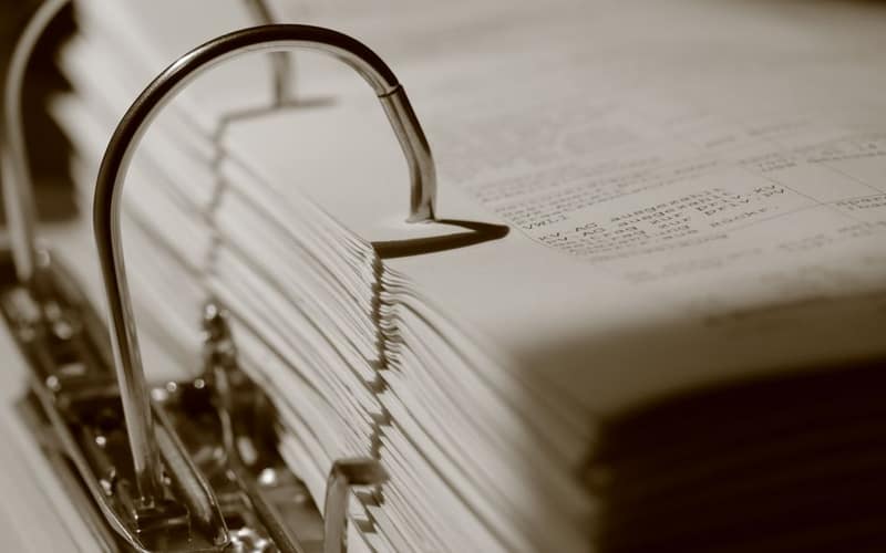 Detailed sepia close-up of a binder filled with documents, emphasizing texture.