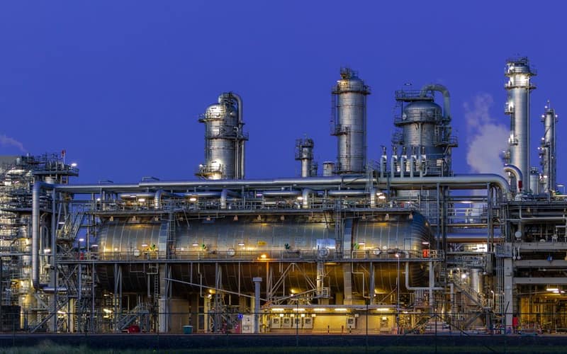 Vista suggestiva di un impianto industriale nello Zuid-Holland, illuminato al crepuscolo contro un cielo azzurro terso.