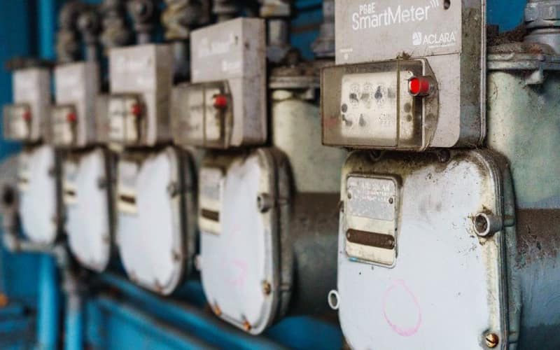 Multiple smart utility meters lined up on a blue industrial wall.