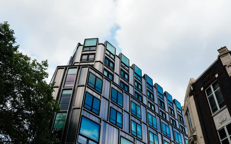 A contemporary building with reflective windows in an urban setting under a cloudy sky.