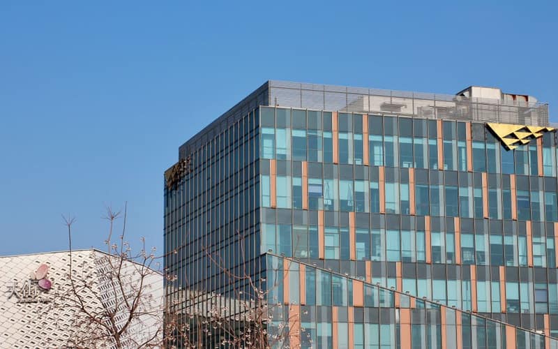 Two modern office buildings with glass facades under a clear blue sky.