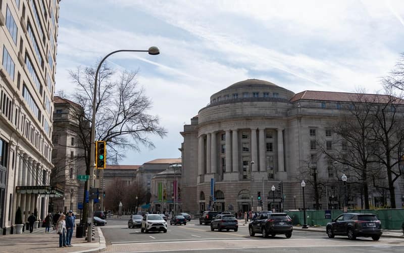 Traffic and pedestrians on a street with historic architecture in Washington DC on a clear day.