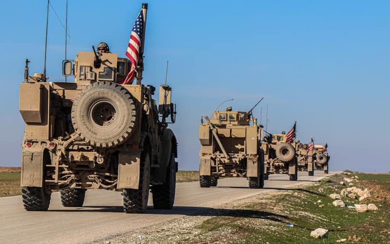 American military convoy driving through rural Syria under a blue sky.