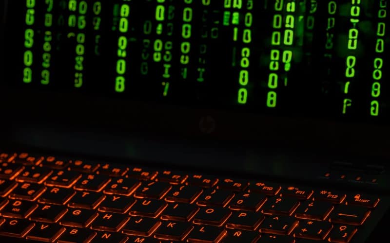 Una tastiera di laptop con retroilluminazione arancione che mostra simboli di codice digitale verde.