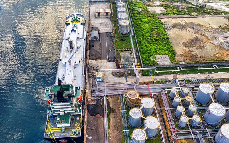 Aerial view of a ship docking at an industrial port with storage tanks in North Jakarta.