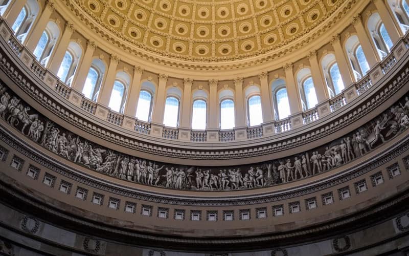 From below of carved stone bas relief frieze and arched windows decorating dome of United States Capitol located in Washington DC