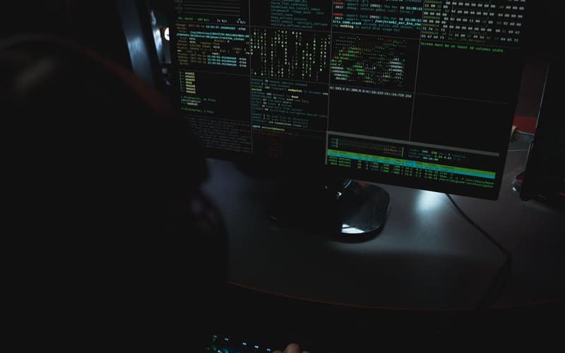 Dark room setup with code displayed on PC monitors highlighting cybersecurity themes.