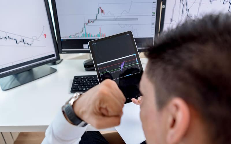A trader confidently viewing stock market charts on multiple monitors in a modern workspace.