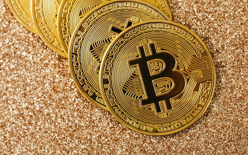 Golden Bitcoin coins arranged on a sparkling glitter surface, symbolizing cryptocurrency and wealth.
