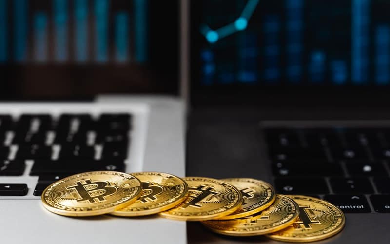 Gold bitcoins placed on laptop keyboards with digital financial graphs in the background.