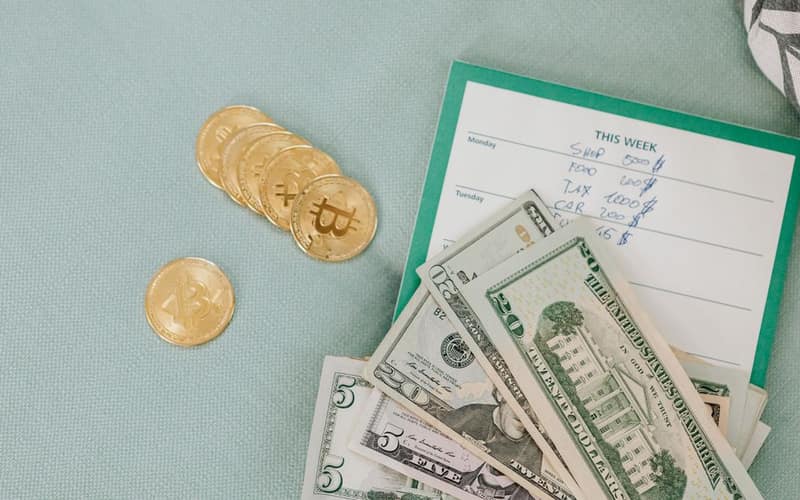 Close-up of U.S. dollars and Bitcoin coins placed on a weekly budget planner, symbolizing modern finance.