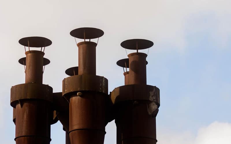 A close-up of three rusted industrial chimneys silhouetted against a clear blue sky.