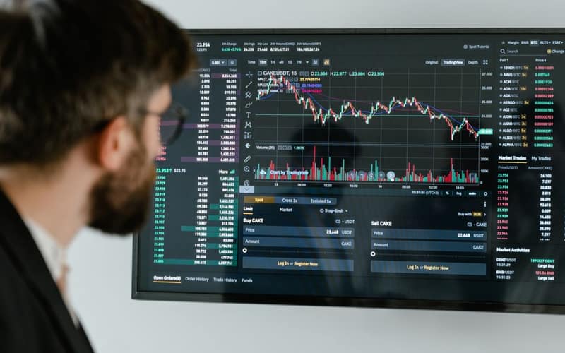 A businessman in a suit looks at a screen displaying stock market charts and data analysis.