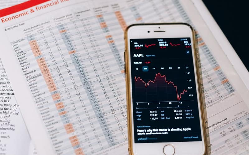 Smartphone displaying stock market data on papers with financial charts.