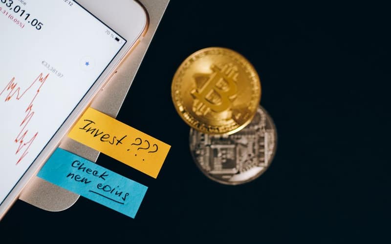 Bitcoin coins and smartphone displaying price chart with investment notes.