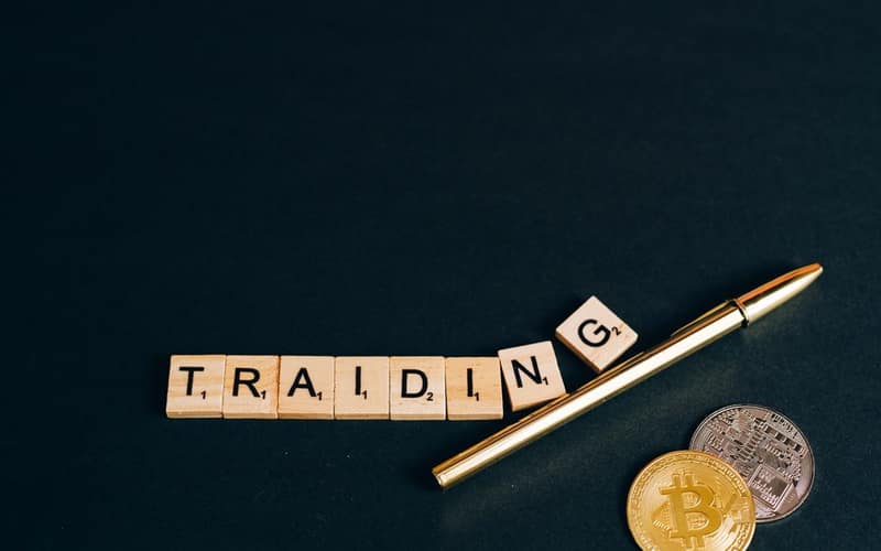 Bitcoin and trading concept shown with coins, pen, and letter tiles on a dark background.