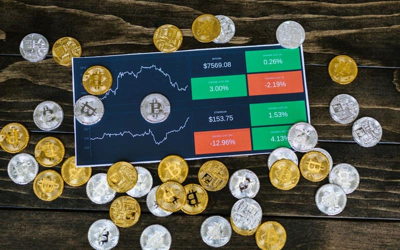 Bitcoin coins scattered around a stock chart on a dark wooden table, symbolizing cryptocurrency investment.