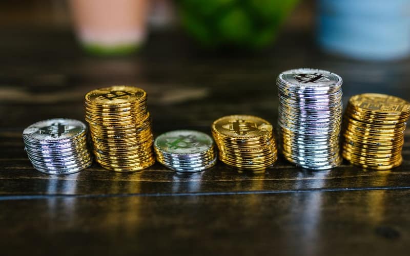 Pile of shiny gold and silver cryptocurrency coins on a wooden table.