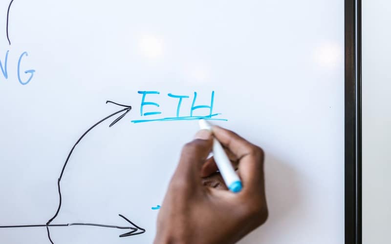 Hand writing 'ETH' on a whiteboard, highlighting Ethereum concept.