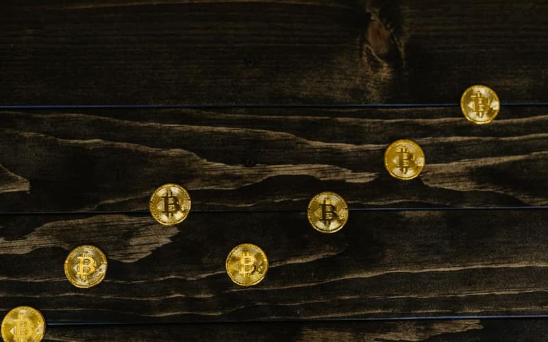 Gold-colored bitcoins arranged diagonally on a dark wooden surface.