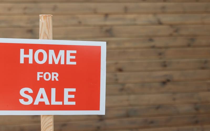 Primo piano di un cartello rosso vendesi contro uno sfondo in legno, ideale per uso immobiliare.