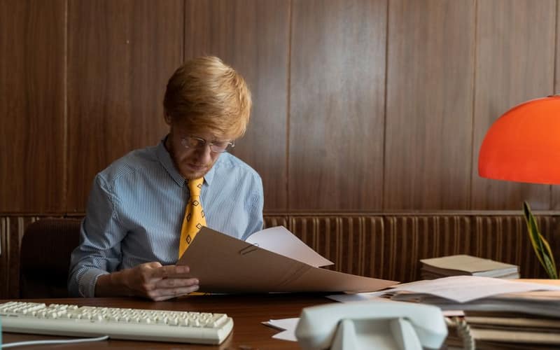 Man in retro office setting reviewing documents under warm light. Ideal for business themes.