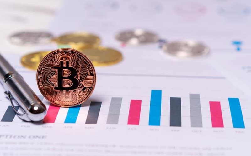 Close-up of a Bitcoin coin placed on financial charts with a pen, symbolizing cryptocurrency and economic analysis.