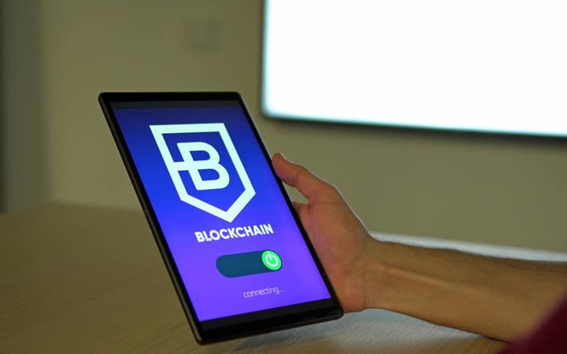 A hand holding a tablet with blockchain logo on screen, showcasing digital technology.